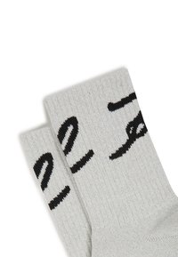 Calcetines grises de tela de punto con un diseño de texto negro. Textura acanalada en la parte superior. El texto aparece en una fuente en negrita, ligeramente curvada.