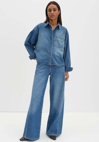 Jeanshemd und Jeans mit weitem Bein in Hellblau. Das Hemd verfügt über eine durchgehende Knopfleiste und eine Brusttasche. Glatte Textur mit kontrastierenden Nähten.