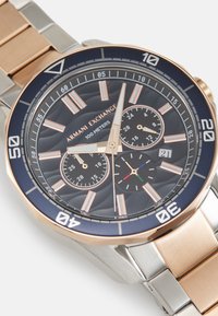 Chronograph-Uhr mit dunkelblauem Ziffernblatt, rosevergoldeten Akzenten, drei kleinen Ziffernblättern, Band aus Edelstahl und Roségold, strukturiertem Gehäuse, 100 Meter wasserdicht.