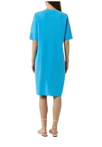 Blaues Leinenkleid mit kurzen Ärmeln, in mittellanger Länge und geradem Schnitt. Einfaches Rückendesign mit einer mittigen Naht. Kombiniert mit beigen Sandalen mit Riemen.