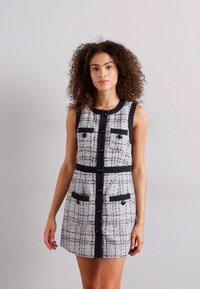 Robe en tweed gris et noir, dotée d'un devant à boutons, de deux poches poitrine et d'une coupe ajustée avec des accents noirs contrastants.