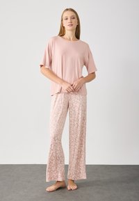 Top corto a maniche corte rosa chiaro abbinato a pantaloni larghi con stampa leopardata beige. Texture liscia, vestibilità comoda e design lungo fino al pavimento.