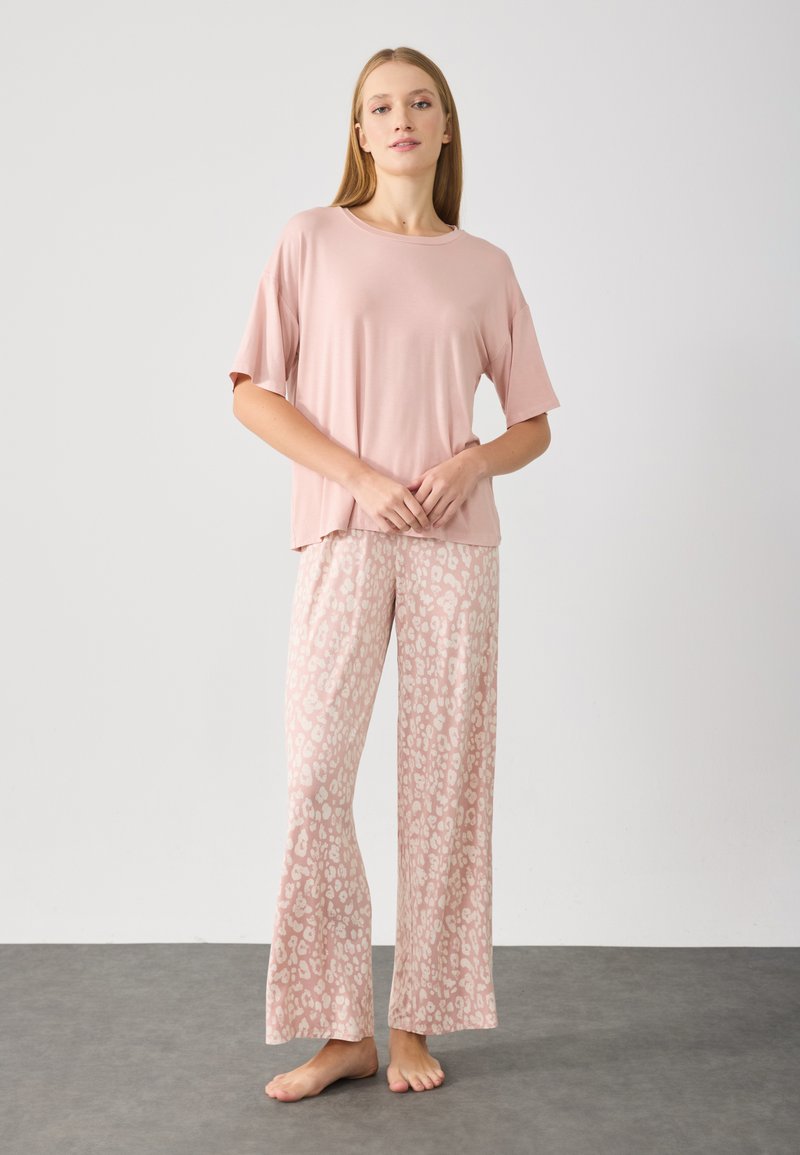 Top de manga corta color rosa claro combinado con pantalones de pierna ancha que presentan un estampado de leopardo beige. Textura suave, ajuste relajado y diseño hasta el suelo.