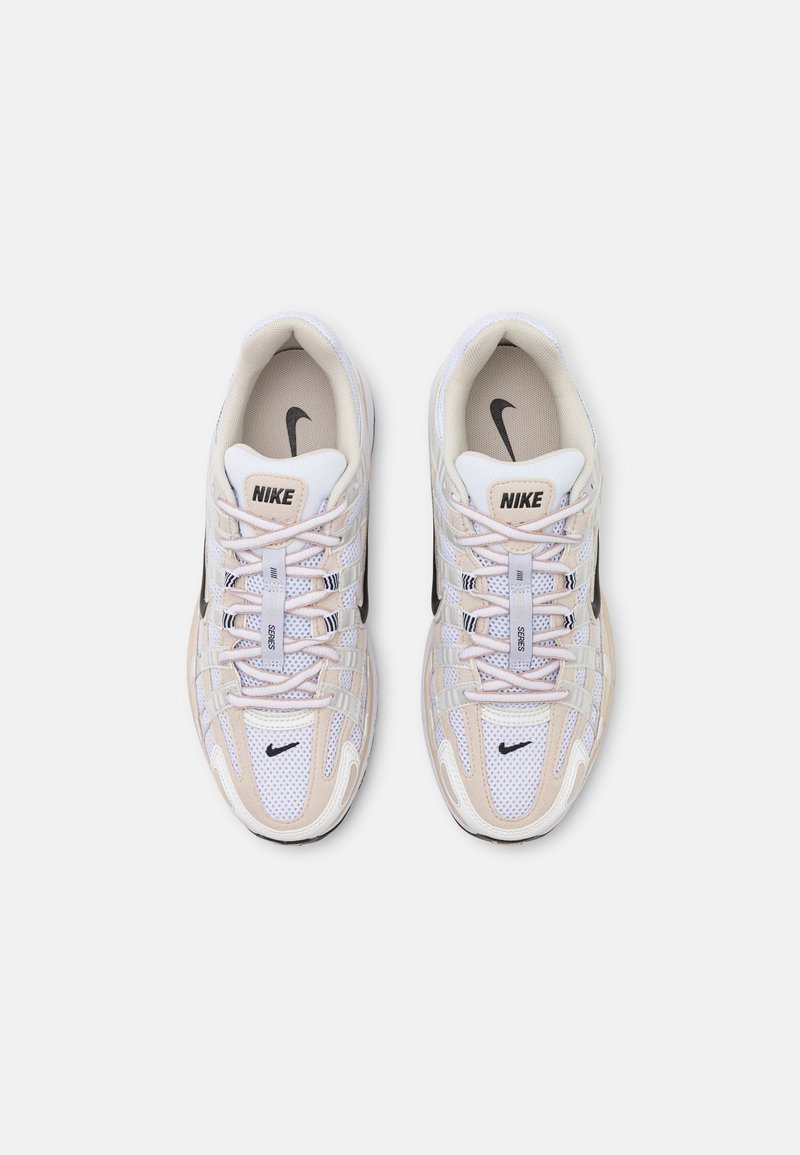 Nike-Sneaker mit einem Obermaterial aus Mesh und synthetischen Materialien, überwiegend weiß mit hellbeigen Akzenten, grauen und schwarzen Details sowie einem Schnürdesign.