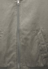 Chaqueta bomber gris con cremallera completa, dos bolsillos laterales, puños acanalados y textura lisa. Diseño sencillo y utilitario.