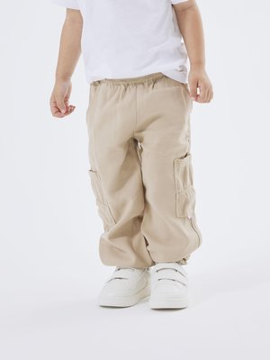 Pantalones cargo beige con cinturilla elástica y bolsillos laterales, combinados con zapatillas blancas con correas de velcro.