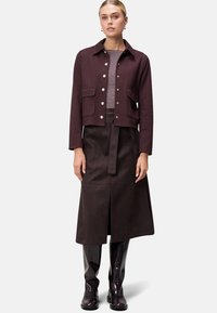 Burgundivörös cropped dzseki ezüst gombokkal, két elülső zsebbel, csíkos toppal és barna midi szoknyával párosítva. Fényes fekete térd fölötti csizmák.