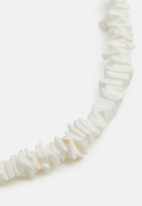 White necklace made of uneven, flattened beads with subtle texture. Each bead varies in shape, creating an organic, flowing design.