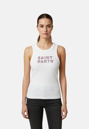 Vrouw met bruin haar dat naar achteren is gebonden, draagt een witte mouwloze top met de tekst "SAINT BARTH" en een zwarte broek en staat tegen een effen achtergrond.