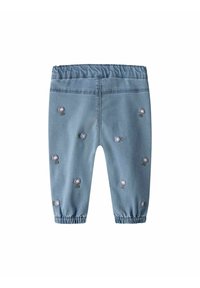 Pantalones de mezclilla azul claro con cintura elástica y flores moradas bordadas esparcidas por toda la prenda. Pierna ajustada con puños recogidos.