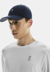 Navy cotton baseball cap with curved brim, featuring a white logo. Worn with a plain white long-sleeve shirt with a small gray logo.