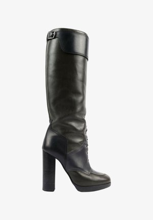 Botte haute en cuir noir à talon haut avec sangle à boucle en haut et détail lacé à l'avant.