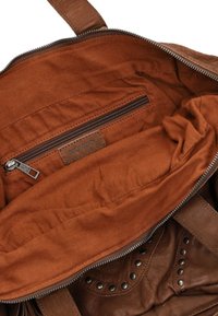 Bruin leren tas interieur met een koperen stoffen voering, voorzien van een ritsvak en metalen studs langs de rand voor accentdetail.