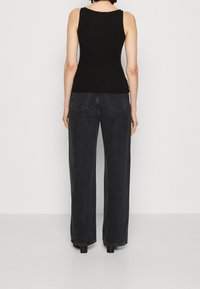 Černý žebrovaný top na ramínka v kombinaci s tmavými džíny s vysokým pasem a širokými nohavicemi. Džíny mají dvě zadní kapsy a čistý lem.