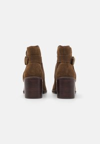 Botas de tobillo de ante marrón con un acento de hebilla metálica, puntera redonda y tacón de bloque de madera, con un acabado texturizado y un diseño de altura media.