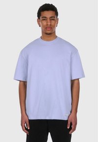 Lys lilla oversized t-skjorte med korte ermer, rund halsutskjæring og lett tekstur. Inkluderer en liten logotag på kanten.