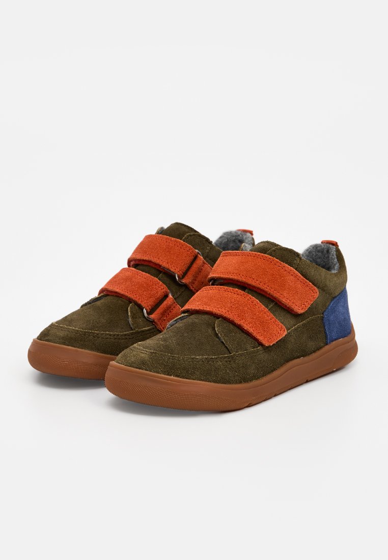 Zapatillas de ante en verde oliva con correas de velcro naranjas, forro gris y acento azul en el talón. Suela de goma con agarre texturizado.