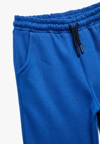 Blå joggingbukser med elastisk talje, justerbar snøre og sidelommer. Fremstillet af blødt, struktureret stof for komfort.
