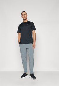 Mustapaita, jossa on tekstuurikuvio, yhdistettynä vaaleanharmaisiin Nike-housuihin. Mustat sneakerit keltaisilla yksityiskohdilla täydentävät urheilullista ilmettä.