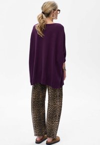 Fioletowy, oversize'owy sweter, luźny krój, teksturowany splot. Para spodni w szerokim kroju w leopardzi wzór z czarnymi akcentami, noszona z brązowymi, płaskimi sandałami.