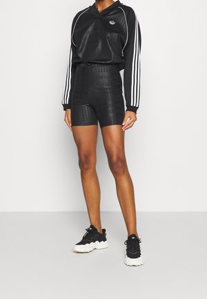 Musta urheilullinen asu, jossa on teksturoitu pitkähihaisen paita valkoisilla raidoilla ja siihen sopivat korkeavyötäröiset shortsit. Yhdistetty mustiin lenkkareihin.