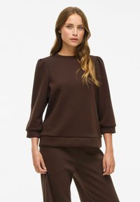 Brun genser med tre fjerdedels puffermer, rund hals og myk tekstur. Enkel design med løs passform og ribbestrikket nederkant.