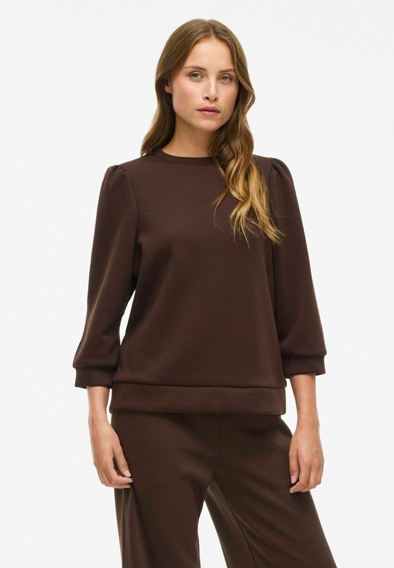 Brun genser med tre fjerdedels puffermer, rund hals og myk tekstur. Enkel design med løs passform og ribbestrikket nederkant.