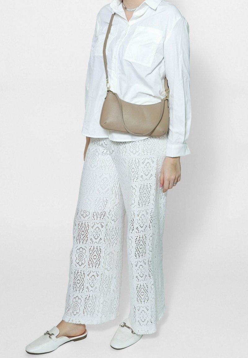 Witte lange mouwen button-up shirt, witte kanten brede broek, beige schoudertas en witte instapschoenen.