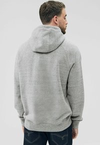 Sudor cu glugă de culoare gri, cu o textură moale, mâneci raglan și glugă căptușită. Prezintă o croială relaxată și manșete și tiv din material rib. 