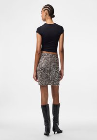 Melnas īsām piedurknēm topiņš, sudraba spīdīgu paillešu mini svārki un melni augstpapēžu zābaki. Gluda auduma un spīdīgu paillešu kombinācija rada teksturētu izskatu.