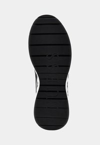 Suola di scarpa in gomma nera con scanalature orizzontali e logo "GUESS" in rilievo, con accenti bianchi sui lati e forma arrotondata.