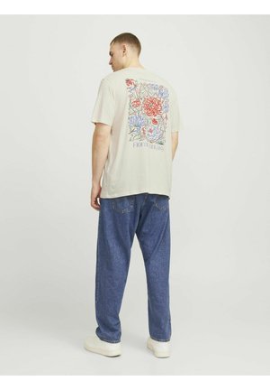 Lichtbeige graphic t-shirt met een kleurrijk bloemenontwerp op de achterkant. Gecombineerd met losse blauwe spijkerbroeken en witte sneakers.