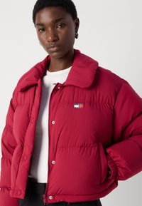 Κόκκινο φουσκωτό μπουφάν με κλασικό γιακά, φερμουάρ και κουμπιά σsnap; διαθέτει κεντητό λογότυπο και ελαστικές μανσέτες.