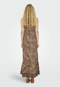 Robe maxi à motifs de feuilles marron avec un corsage smocké et une dentelle au niveau de l'ourlet. Le mannequin se tient de dos face à la caméra, portant des chaussures à plateforme marron.