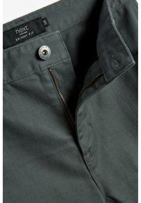 Dark gray skinny fit trousers with a zip fly, metal button closure, and stitching details. Made of a smooth fabric, showcasing a sleek design.
