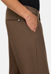 Rudos kelnės iš lygaus audinio su šonine kišene, ant kurios yra mažas logotipo ženklelis. Prigludusi forma, subtilūs klostės detalės.