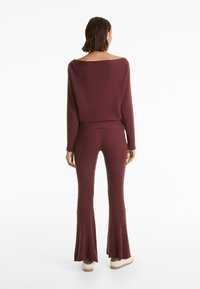 Bordeaux-rot gerippter Strickpullover und passender fließender Hosenanzug, mit lockerer Passform, schulterfreiem Design und strukturiertem Stoff.