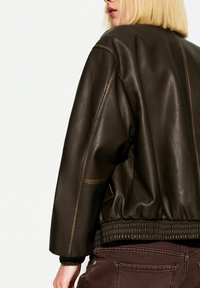 Braune Leder-Bomberjacke mit gerippten Bündchen und Saum; glatte Textur; sichtbare Nähte entlang der Schultern; lässige Passform.