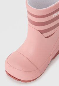 Bota de lluvia de goma rosa con superficie texturizada, que presenta franjas horizontales de un rosa más oscuro y una puntera redondeada. Forro suave visible en la parte superior.
