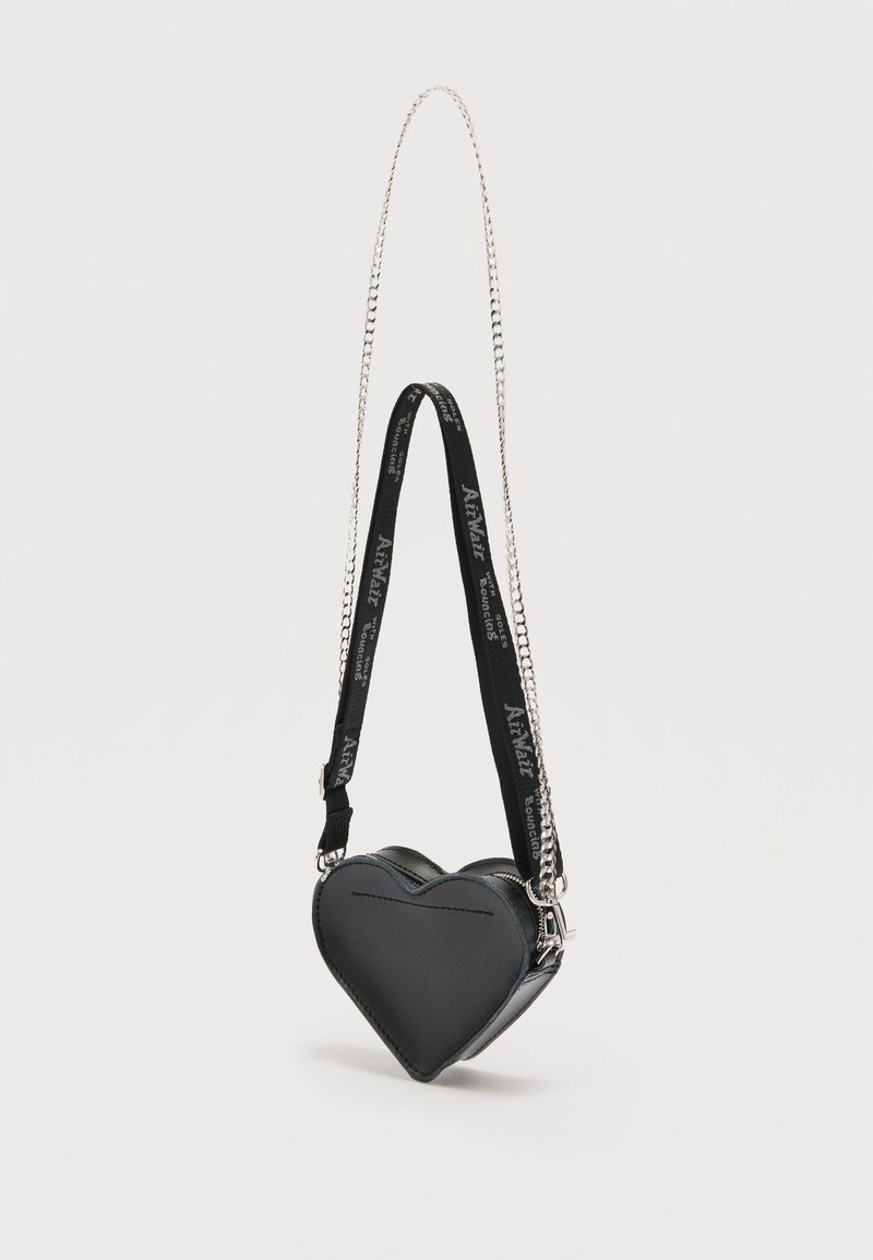 Black heart-shaped handbag with silver chain and black fabric strap featuring white text, suspended against a plain light background.