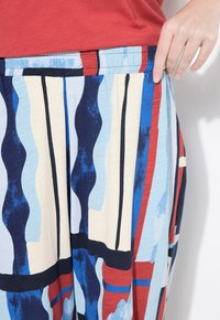 I pantaloni a gamba larga, colorati e con motivo, presentano strisce blu, rosse e crema, con una vita elasticizzata e un tessuto morbido e testurizzato.