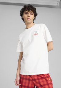 Witte katoenen t-shirt met een klein grijs Puma-logo en rode "PUMA" tekst op de borst, gecombineerd met rood geruite shorts.