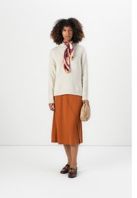 Beige gestrickter Pullover mit Rautenmuster, orangefarbenen Wickelrock, gemusterter Seidenschal, braunen Slippern und einer beigen Clutch.