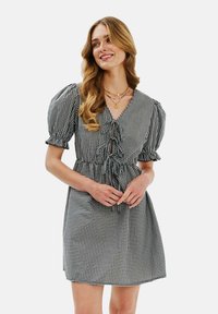 Čierno-biele kárované šaty s krátkymi puff rukávmi, výstrihom do V, volánikovým detailom vpredu, stiahnutým pásom a dĺžkou nad kolená.