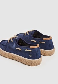 Zapatos de barco de ante marino con cordones de cuerda trenzada, detalles en marrón claro y suela de yute texturizada. Costuras robustas y detalle del logotipo en el lateral.