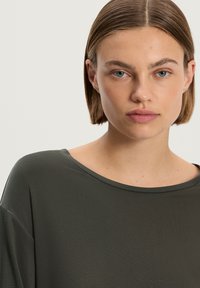 Top verde scuro, morbido e dalla vestibilità ampia, con scollatura larga, maniche corte e dettagli minimi.