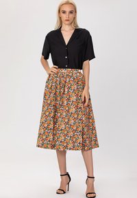Haut noir à manches courtes avec boutons associé à une jupe midi à imprimé floral avec des fleurs orange et roses sur un fond noir.