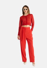 Cardigan rosso corto con maniche lunghe e chiusura a bottoni abbinato a pantaloni rossi a vita alta con vita cinture e pieghe.
