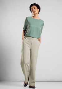 Ljusgrön, lös silkig topp med korta ärmar, kombinerad med högmidjade, vida beige byxor. Svarta platta skor. Enkelt mönster, inga mönster.