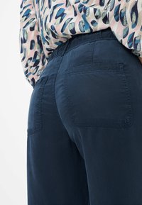 Pantalons légers bleu marine avec une texture lisse, taille élastique et deux poches arrière. Les pantalons sont associés à un chemisier à motif.
